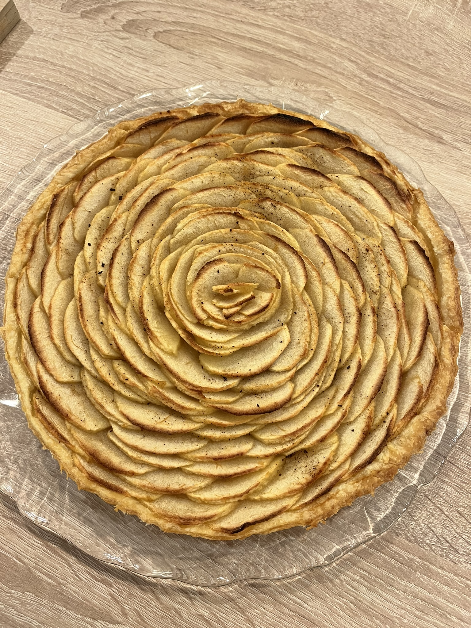 Tarte aux pommes dorée, avec des lamelles de pommes disposées en rosace sur une pâte feuilletée, vue de dessus.