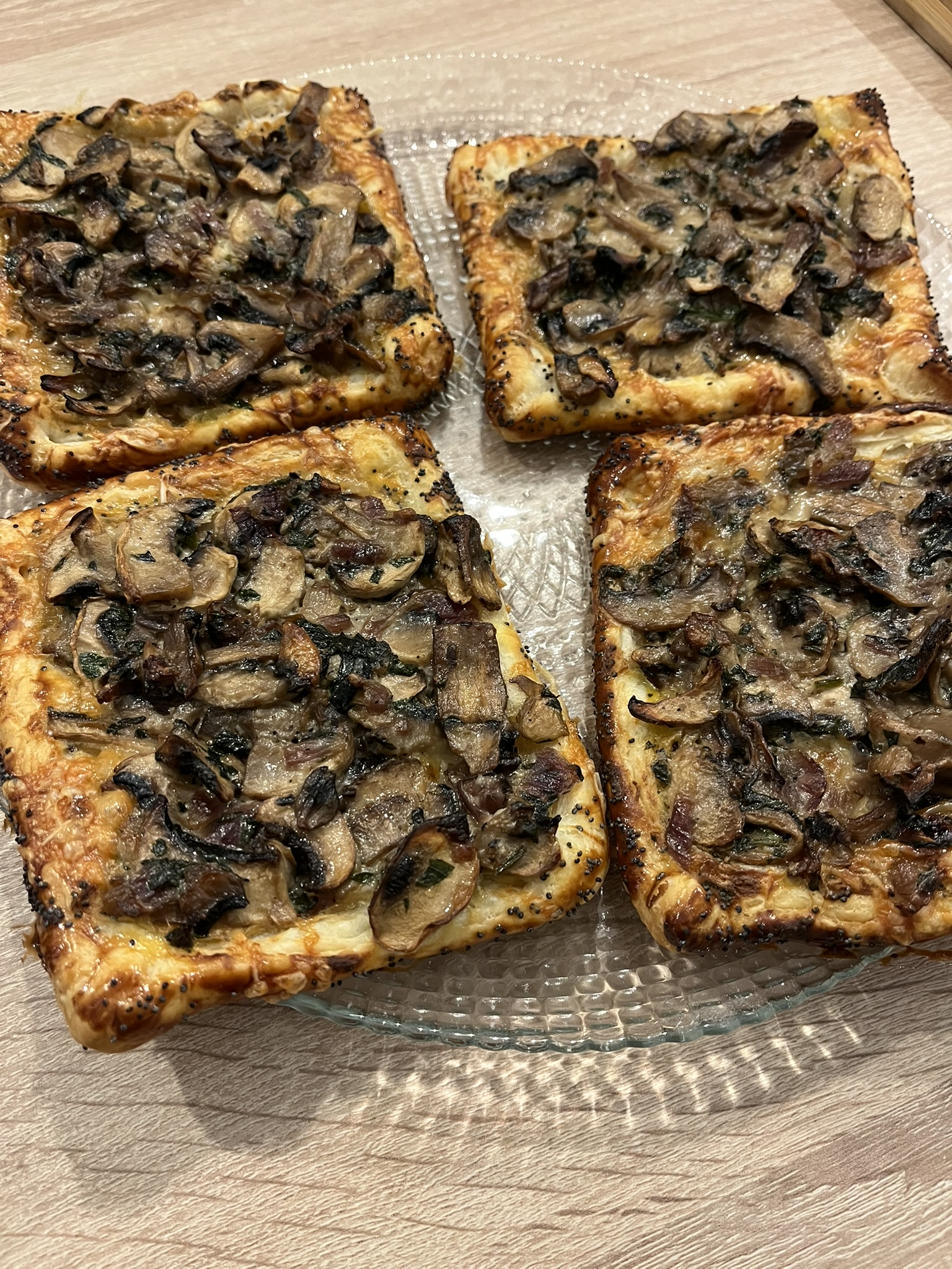 Quatre feuilletés aux champignons et au comté, dorés et croustillants, dressés dans une assiette transparente.
